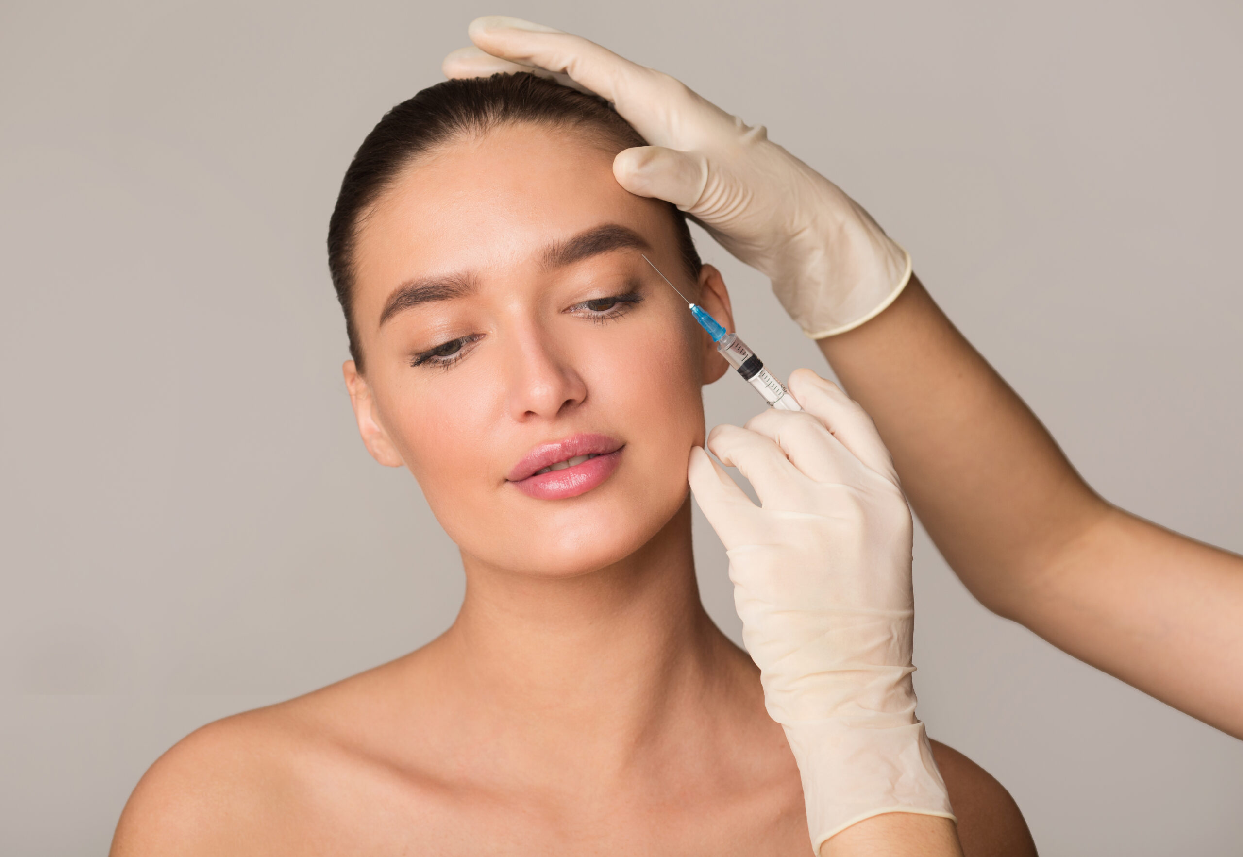 Plastic Surgery And Beauty Injection Concept. Young Woman Receiving Botox For Wrinkles, Isolated Over Studio Wall